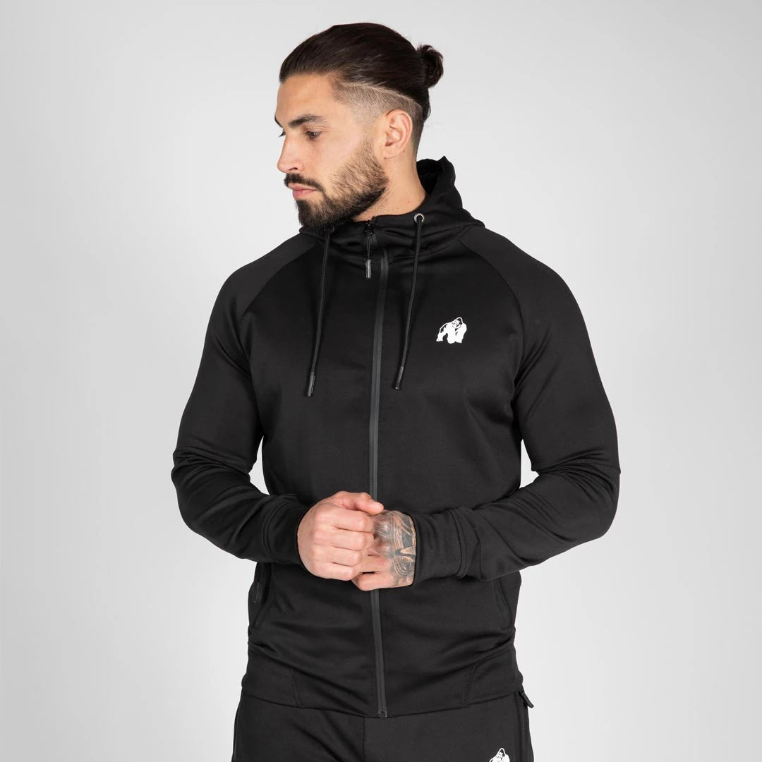 Mies pukeutuneena mustaan, hupulliseen Gorilla Wear Sullivan Track Jacket Black -treenitakkiin valkoisella logolla., kuva 1/7