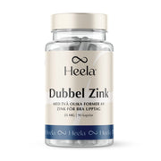 Heela Dubbel Zink 60 caps i en transparent burk med vita kapslar, beigefärgad etikett och blå bottenrand.
